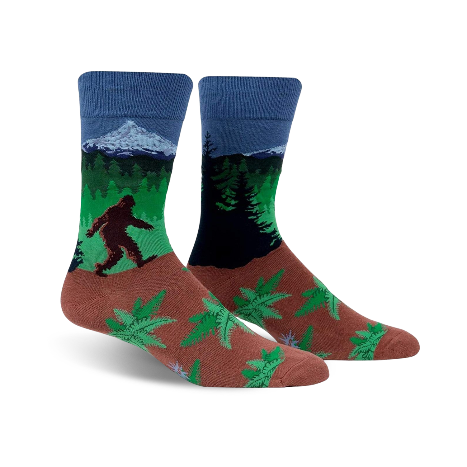 A pair of crew socks showcasing Bigfoot trekking through a forest landscape with a mountain in the background. The socks are predominantly blue, green, and brown, with a fern pattern at the bottom.