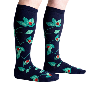 A pair of dark blue knee-high socks with a repeating pattern of red ladybugs and green leaves.