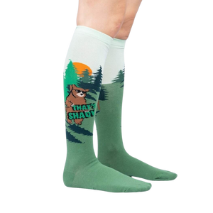 A pair of green knee-high socks with a pattern of dark green pine trees and brown Bigfoot.