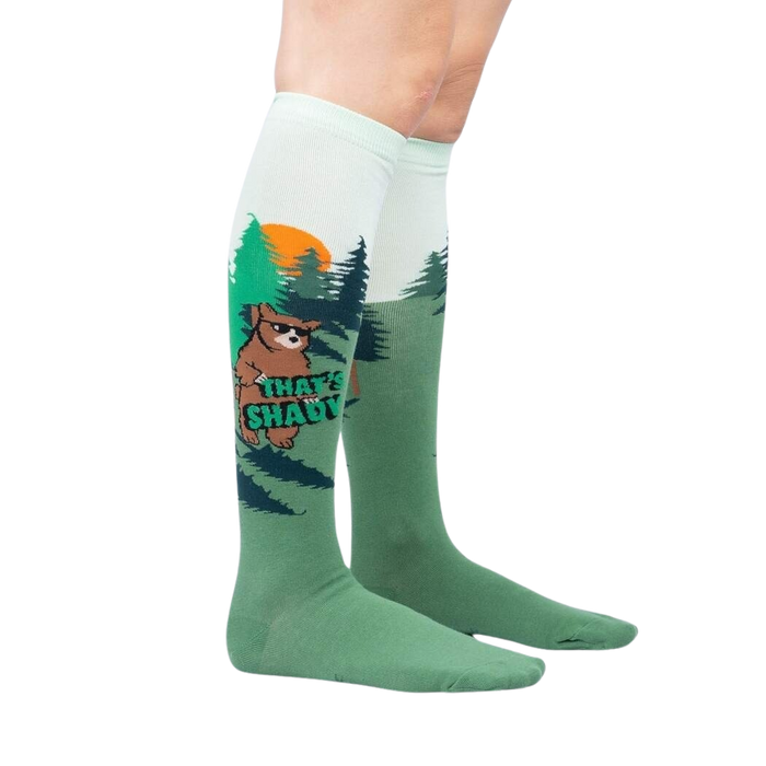 A pair of green knee-high socks with a pattern of dark green pine trees and brown Bigfoot.