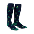 Pair of navy blue knee-high socks with a repeating pattern of green Bigfoot figures hidden amongst lime green and darker green Christmas trees.