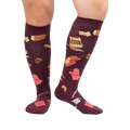 Lifestyle shot of 'Bake at 350' knee-high socks in burgundy on a person's legs against a white background.