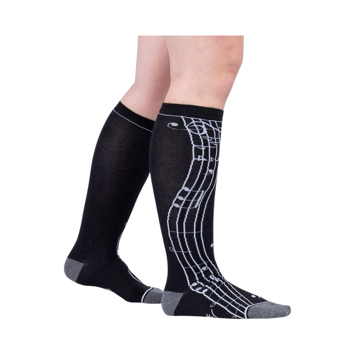 Lifestyle shot: A person's legs wearing the black knee-high musical note socks.