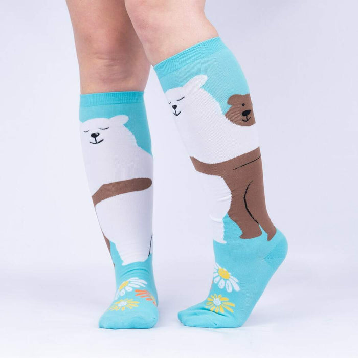 A pair of blue knee-high socks with a brown bear holding a bouquet of white daisies on each sock.