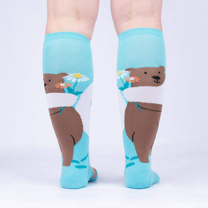A pair of blue knee-high socks with a brown bear holding a bouquet of white daisies on each sock.