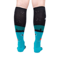 Rear view of the socks highlighting the full design. The socks are teal and black and glow in the dark.