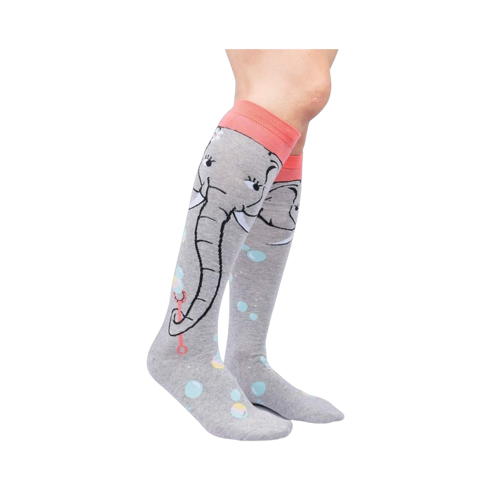 Lifestyle shot: Model wearing a pair of grey and coral knee-high socks with an elephant and bubble design.