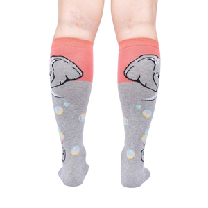 A pair of gray and pink knee-high socks with an elephant on the back of each sock. The elephant is gray with a pink ear and a pink flower in its hair.