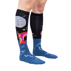 A pair of black knee-high socks with a blue section at the ankle and a pink heel and toe. There is a pattern of stars and moons on the black section and a mountain pattern on the blue section.
