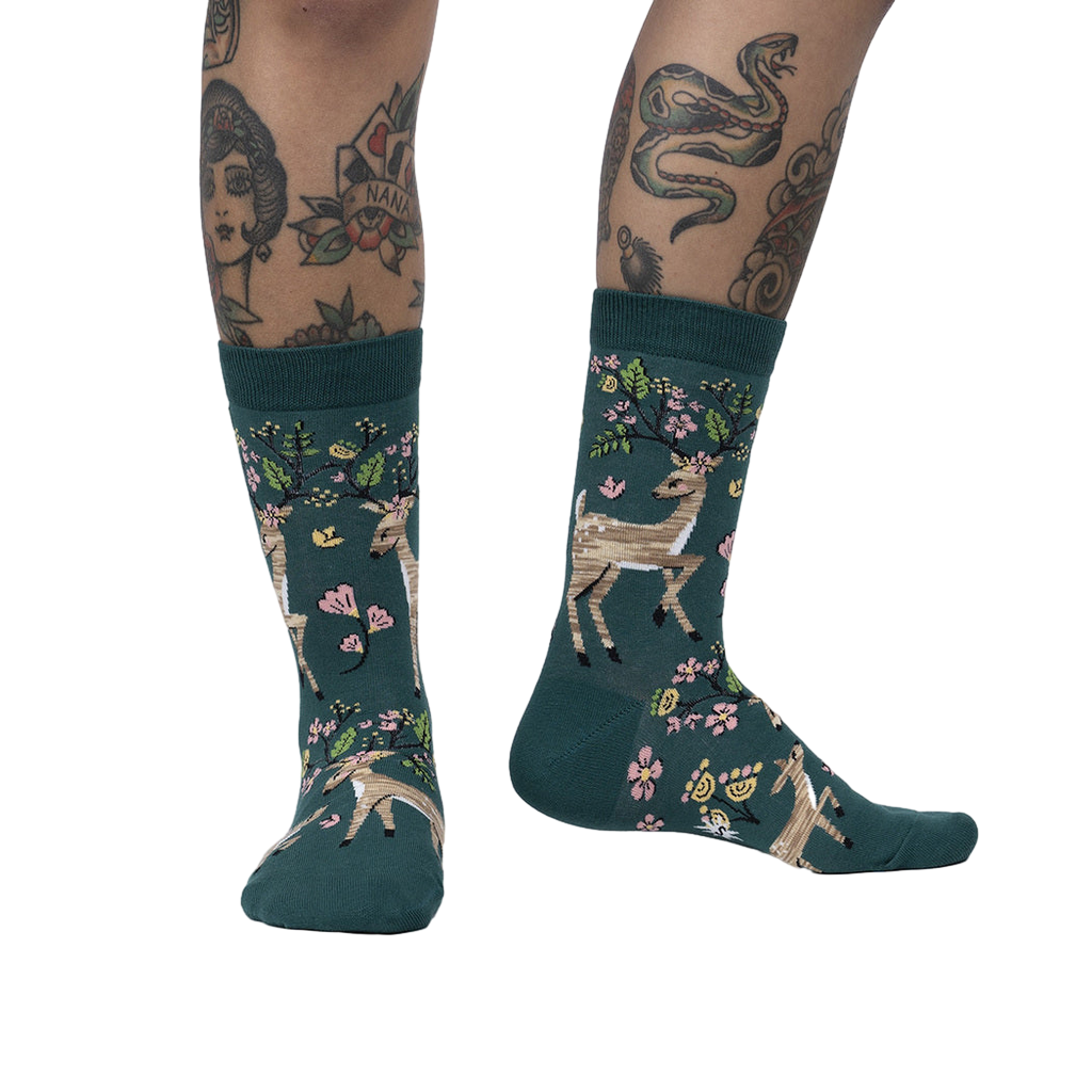 Lifestyle shot of model wearing teal crew socks with deer and flower design.