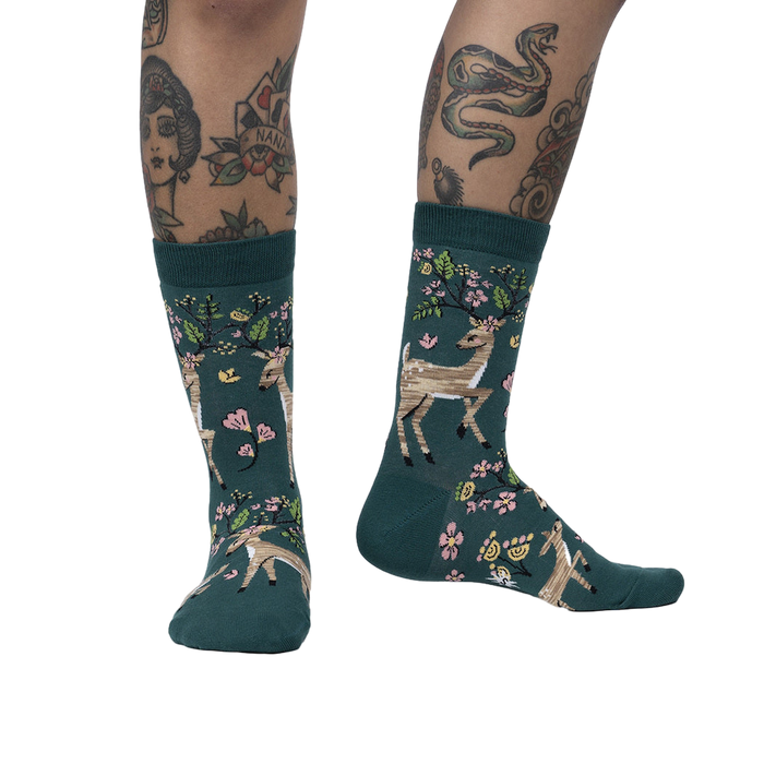 Lifestyle shot of model wearing teal crew socks with deer and flower design.