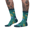 Lifestyle shot showing the Plant Mom socks on a woman's legs. The socks are green with a fun plant design.