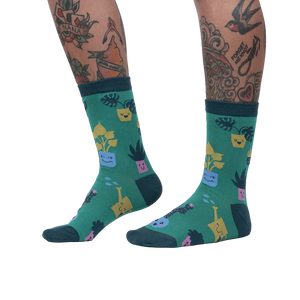 Lifestyle shot showing the Plant Mom socks on a woman's legs. The socks are green with a fun plant design.