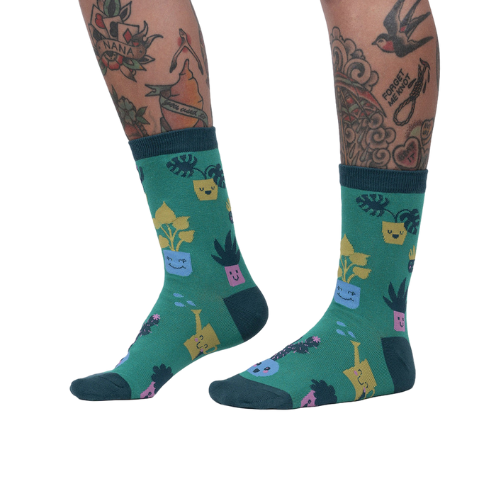 Lifestyle shot showing the Plant Mom socks on a woman's legs. The socks are green with a fun plant design.
