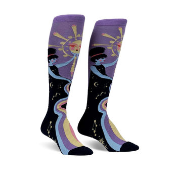 Pair of women's knee-high socks. Purple and black with a celestial design featuring two women, a sun, and a rainbow river of stars.