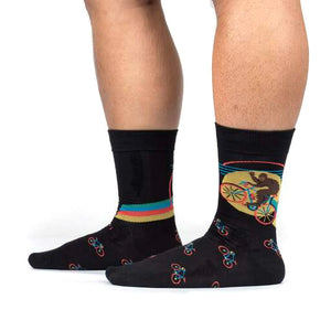 A pair of black socks with a colorful pattern of bigfoot riding a bicycle.