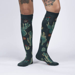 A pair of dark green knee-high socks with a pattern of red and green cacti.