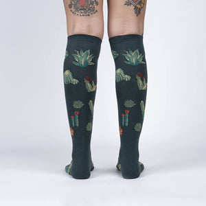A pair of dark green knee-high socks with a pattern of red and green cacti.