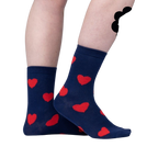 Close-up on a person's legs wearing navy blue crew socks with red fuzzy hearts.