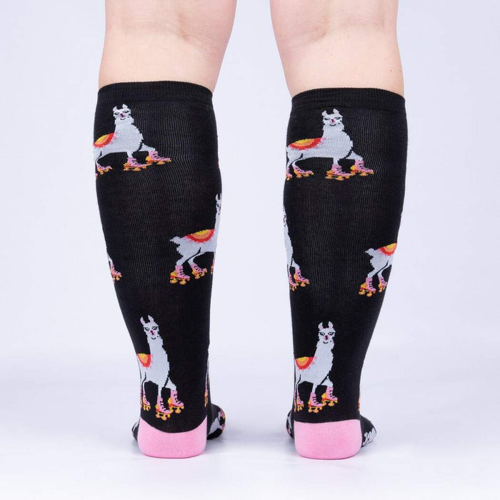 A pair of black knee-high socks with a pattern of cartoon llamas wearing roller-skates in pink, yellow, blue and orange. The socks are shown on the back of a person's legs from the knees down.