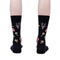 Rear view of the 'Let That Shiitake Go' socks on a model's feet.  The socks are black with a mushroom and pun design.