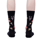 Rear view of the 'Let That Shiitake Go' socks on a model's feet.  The socks are black with a mushroom and pun design.