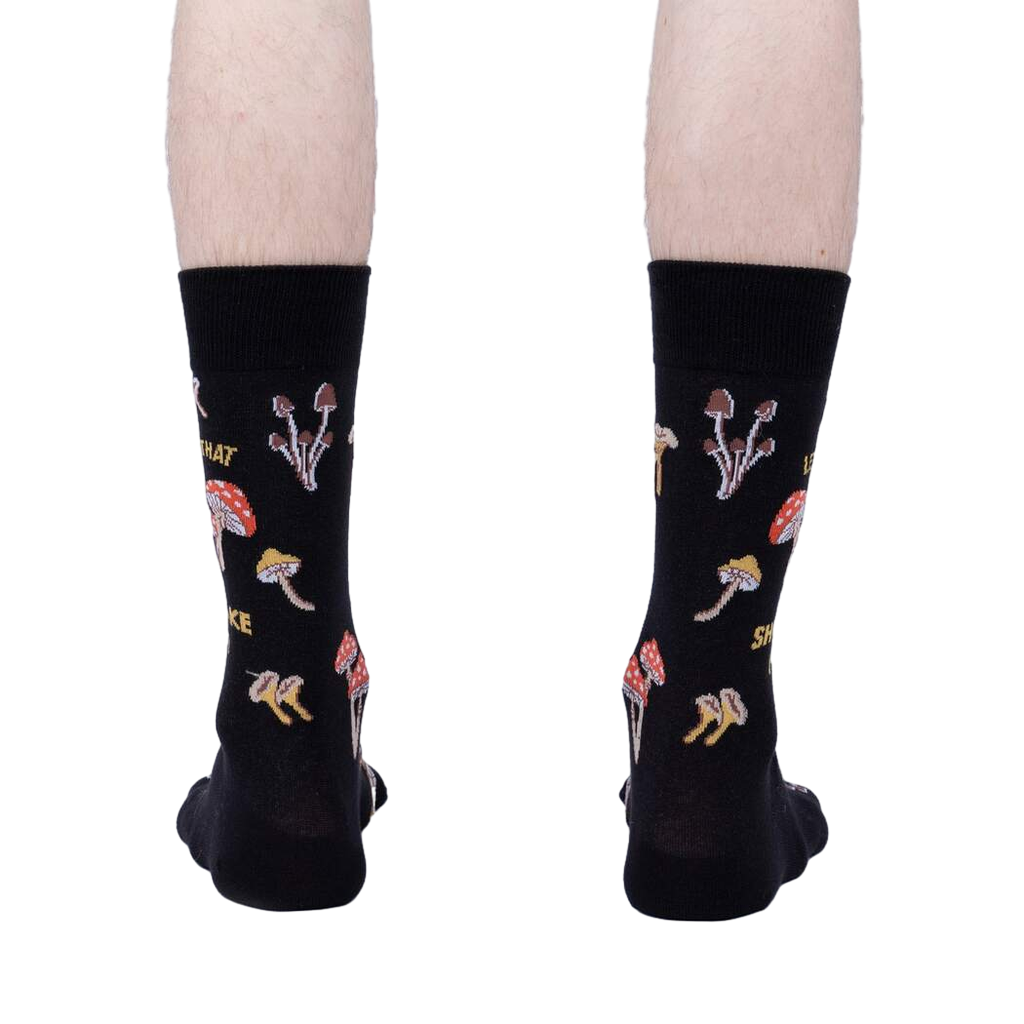 Rear view of the 'Let That Shiitake Go' socks on a model's feet.  The socks are black with a mushroom and pun design.