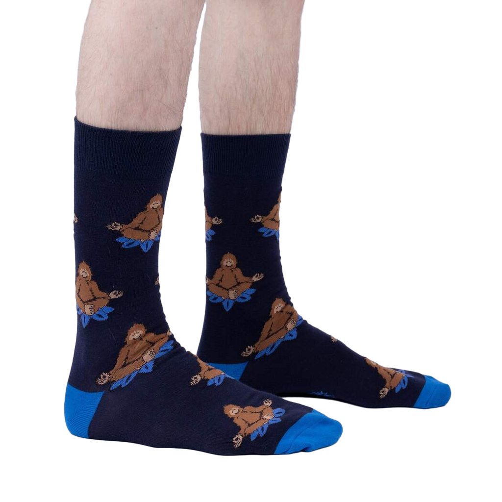 Lifestyle shot showing the Meditating Bigfoot socks on a person's legs against a light grey background.