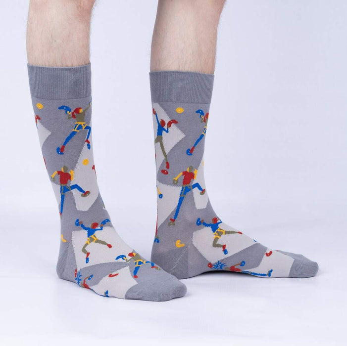 A pair of gray socks with a pattern of rock climbers on them. The climbers are wearing brightly colored clothes and are climbing up a rock wall.