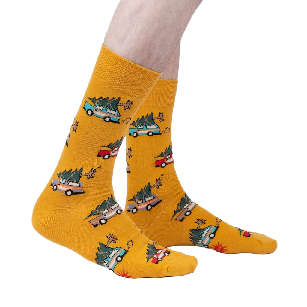 Lifestyle shot of model wearing mustard yellow crew socks featuring cars carrying Christmas trees.