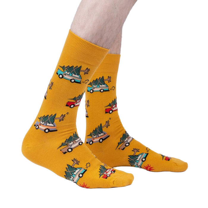 Lifestyle shot of model wearing mustard yellow crew socks featuring cars carrying Christmas trees.