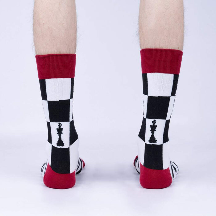 A person is shown wearing a pair of black, white, and red socks. The socks have a chessboard pattern with a black chess king on a white background on the leg portion and a red heel and toe.