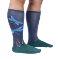 Lifestyle shot of model wearing a pair of teal and navy blue knee-high socks with a dragonfly design.