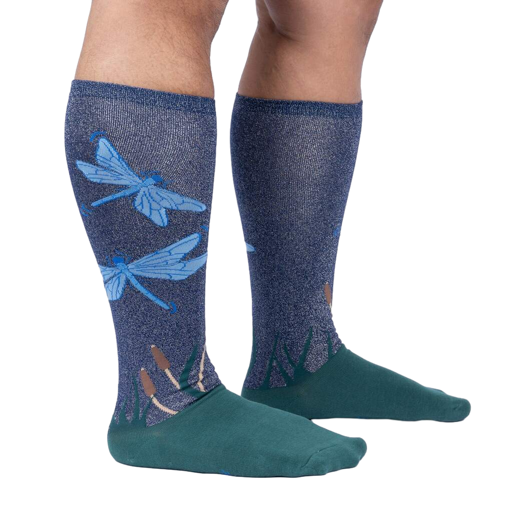 Lifestyle shot of model wearing a pair of teal and navy blue knee-high socks with a dragonfly design.