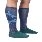 Lifestyle shot of model wearing a pair of teal and navy blue knee-high socks with a dragonfly design.