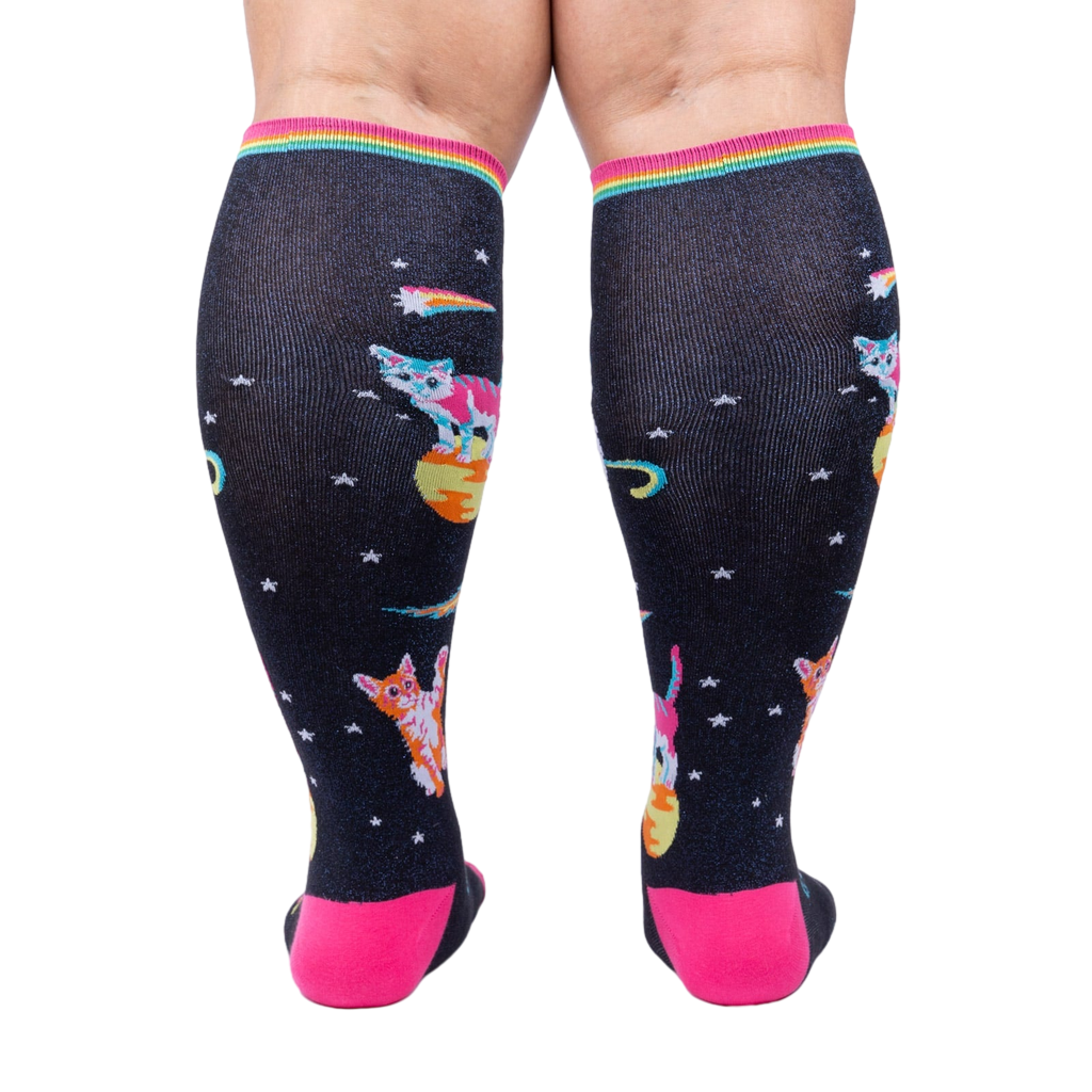 Rear view of Space Cat knee-high socks on a person's legs.  Full view of the sock pattern and bright pink heel.