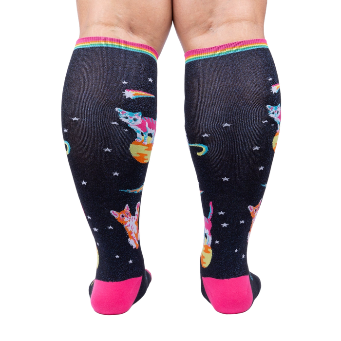 Rear view of Space Cat knee-high socks on a person's legs.  Full view of the sock pattern and bright pink heel.