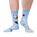 Lifestyle shot of a person wearing the light blue crew socks with cat and pill bottle design.