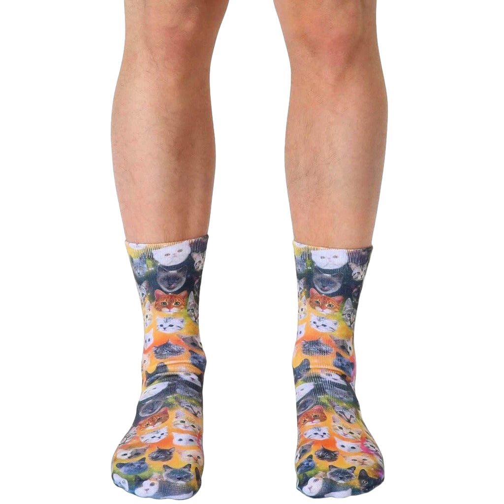 Crew socks showcasing a vibrant galaxy of adorable cat faces in various colors on a yellow-orange background. [lf]