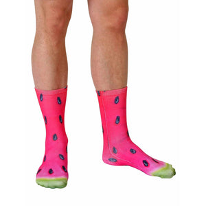 A person is shown wearing a pair of watermelon socks. The socks are pink with black seeds and a green rind at the toes.