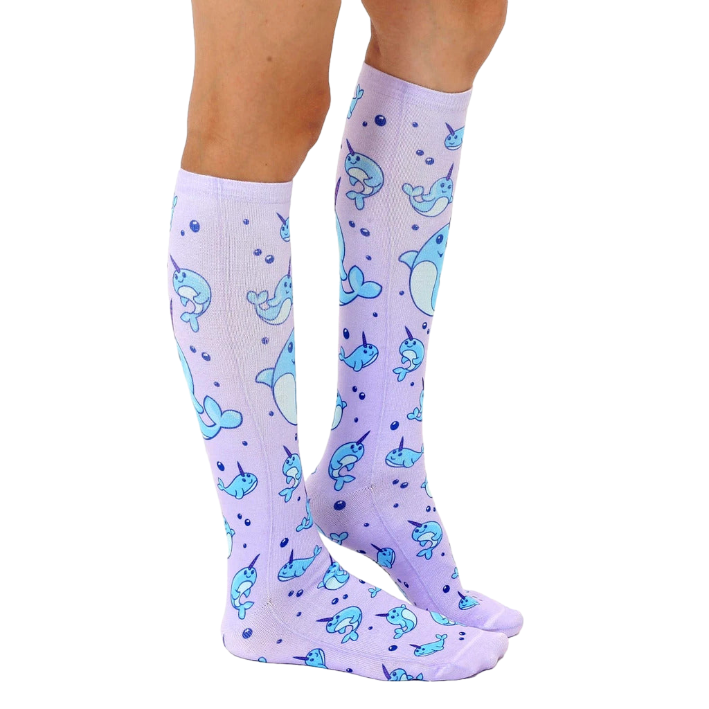 Lifestyle shot: Model wearing a pair of lavender knee-high narwhal socks. [lf]