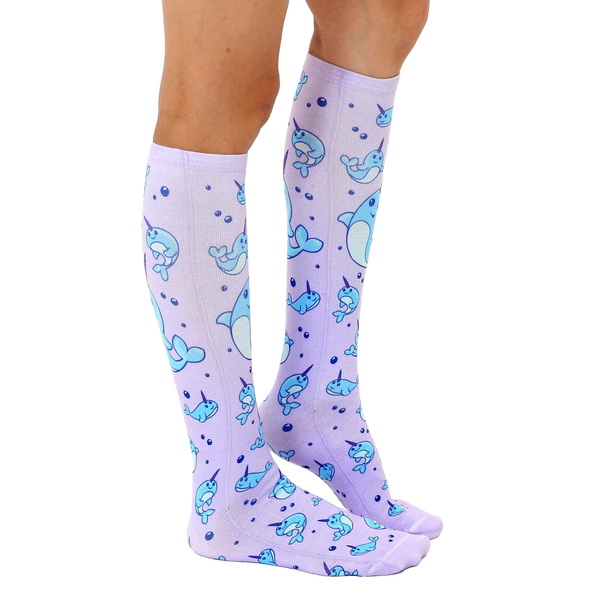 Lifestyle shot: Model wearing a pair of lavender knee-high narwhal socks. [lf]