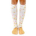 A pair of women's knee-high socks with a whimsical ice cream cone design.  The socks are predominantly white with pastel rainbow sprinkles and a waffle cone pattern at the toes. [lf]