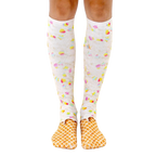 A pair of women's knee-high socks with a whimsical ice cream cone design.  The socks are predominantly white with pastel rainbow sprinkles and a waffle cone pattern at the toes. [lf]