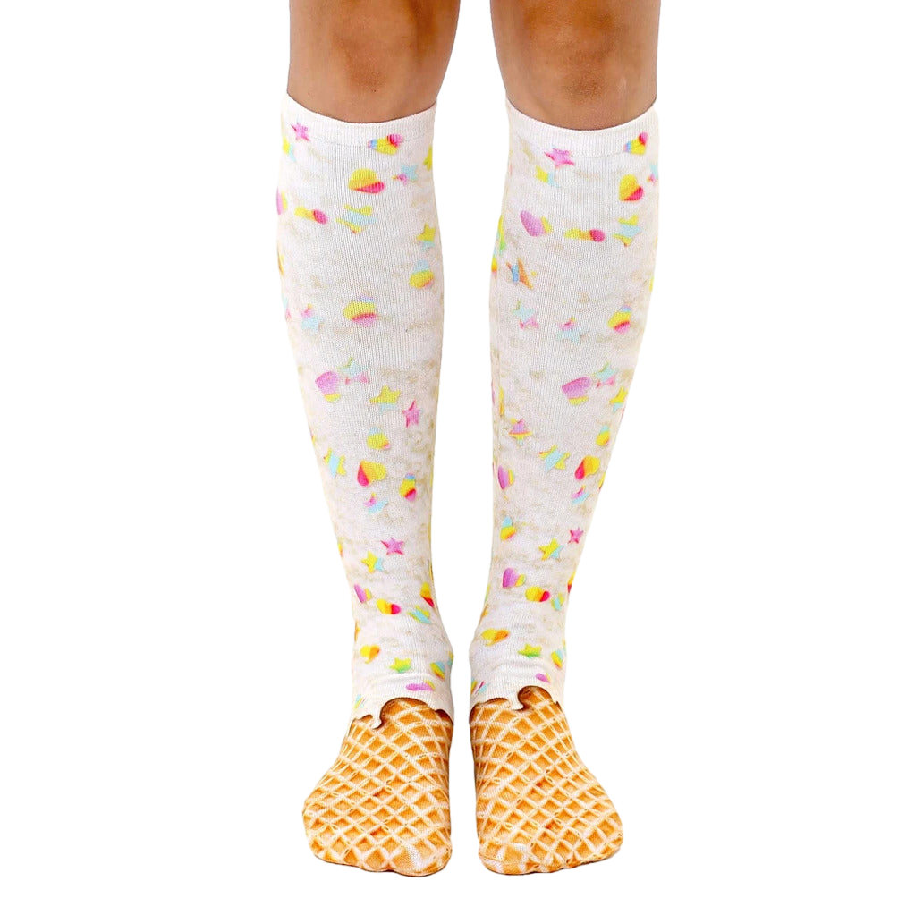 A pair of women's knee-high socks with a whimsical ice cream cone design.  The socks are predominantly white with pastel rainbow sprinkles and a waffle cone pattern at the toes. [lf]