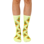 A pair of crew socks in pastel yellow with a repeating pattern of cartoon avocados surfing on their halves. [lf]