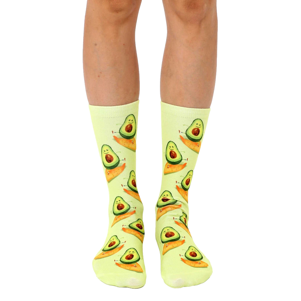 A pair of crew socks in pastel yellow with a repeating pattern of cartoon avocados surfing on their halves. [lf]
