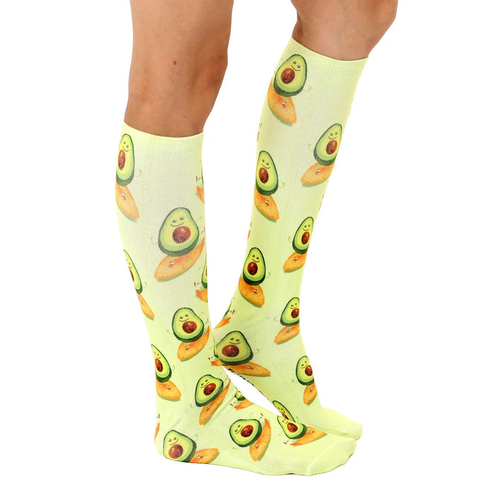 Light green knee-high socks with an all-over pattern of cartoon avocados on yellow surfboards.
