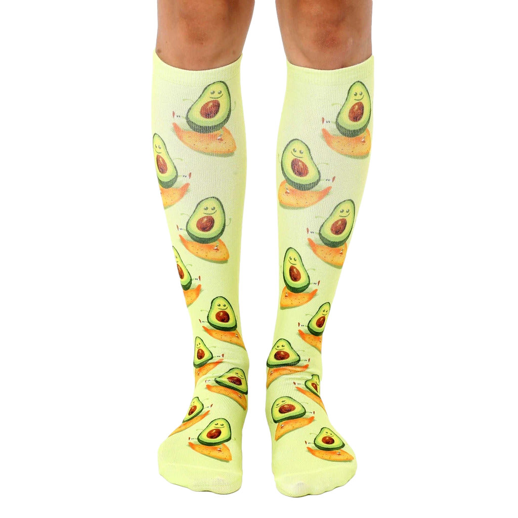 Pair of light green knee-high socks with a repeating pattern of cartoon avocados surfing. [lf]