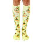Pair of light green knee-high socks with a repeating pattern of cartoon avocados surfing. [lf]